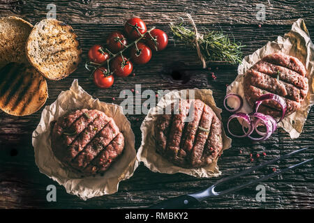 Materie gli hamburger sul tavolo di legno con cipolla Pomodoro erbe aromatiche e spezie. Foto Stock