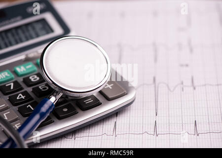 Ecg con uno stetoscopio e calcolatrice che mostra il costo delle cure sanitarie. Close up Foto Stock