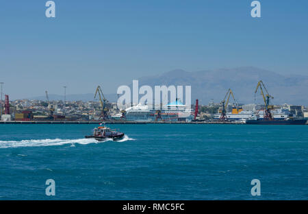 Pilota di vele di imbarcazioni attraverso le onde nel porto di Heraklion sullo sfondo di montagna e le infrastrutture del porto (Grecia) Foto Stock
