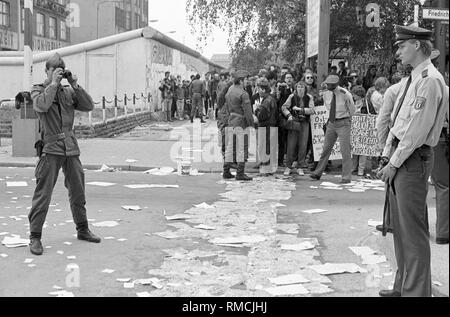 Gli avversari del censimento 1987 stick di decine di migliaia di moduli di registrazione per il Muro di Berlino durante una spettacolare campagna presso il Checkpoint Charlie punto di incrocio, un GDR di guardia di frontiera fotografie la scena come a Berlino Ovest la polizia cerca di fermare l'azione. Foto Stock