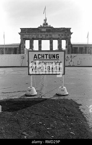 Vista sopra la parete sulla Porta di Brandeburgo con il segno "Attenzione siete lasciando Berlino Ovest ora'. Foto Stock