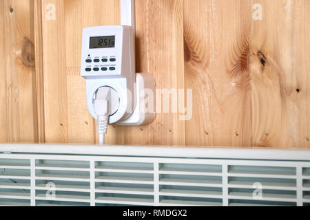 Lavoro elettrico bianco termoconvettore collegato al timer presa di alimentazione azionata in casa intelligente sistema contro la parete di legno all'interno camera vista laterale vista dettagliata Foto Stock