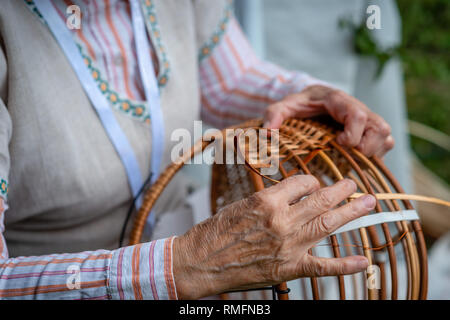 Vecchia donna in costume nazionale rendi locale cesto in vimini. Artigianato tradizionale concetto. Lettonia - Immagine Foto Stock