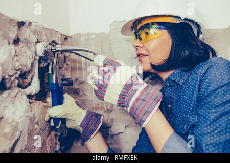Close up idraulico femmina in guanti con chiavi riparazioni i tubi in bagno. La riparazione di tubi, valvole, contatori d'acqua. Foto Stock