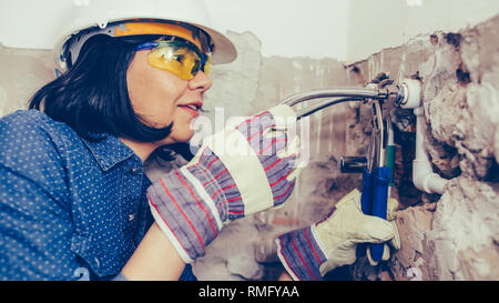 Costruzione femmina lavoratore in guanti con chiavi riparazioni i tubi in bagno. Foto Stock