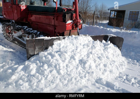 Rosso trattore diesel pulisce la strada dalla neve in un paese di campagna su una luminosa giornata soleggiata vista laterale vista dettagliata Foto Stock