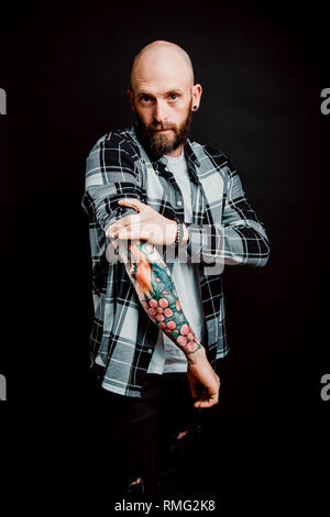 Barbuto tanga glabre nella camicia con tatuaggi sui bracci su sfondo nero Foto Stock
