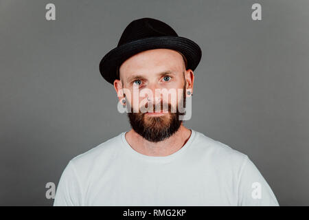 Barbuto tanga glabre in t-shirt e hat su sfondo nero Foto Stock