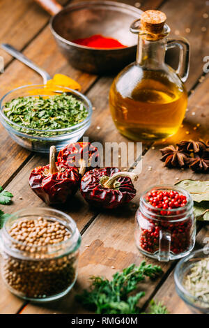 Un assortimento di spezie ed erbe aromatiche e una bottiglia di olio immesso sul piano portapaziente in legno Foto Stock