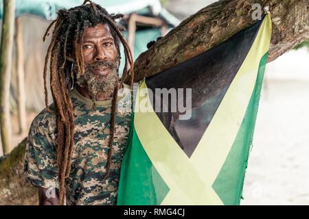 Americano africano maschio barbuto con dreadlocks holding Bandiera della Giamaica vicino a tree Foto Stock