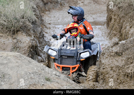 Padre e figlio a cavallo di un Quad/ATV attraverso un foro di fango Foto Stock