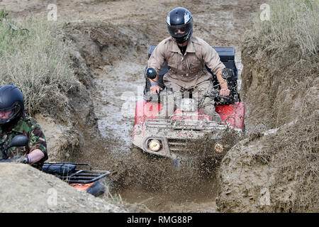 Uomini a cavallo di un Quad/ATV attraverso un foro di fango Foto Stock