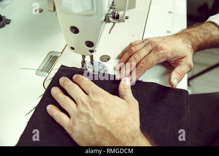 L'uomo le mani dietro la cucitura. Workshop di pelle. Vintage tessili industriali. L'uomo nelle femmine di professione. La parità tra i sessi concept Foto Stock