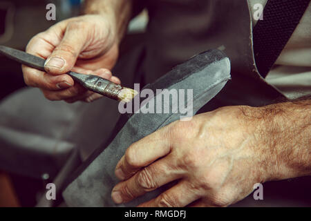 Calzolaio rende le scarpe per gli uomini. Egli le macchie di liquido speciale con un pennello. L'uomo nelle femmine di professione. La parità tra i sessi concept Foto Stock