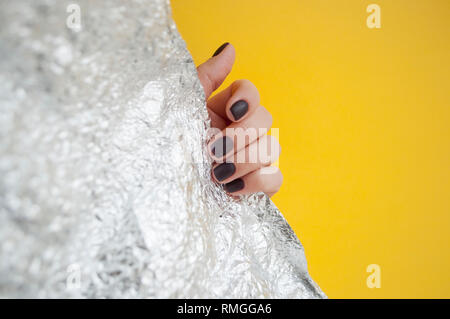 Giovane donna la mano con una bella manicure su giallo e metallica sfondo lucido con copyspace. Foto Stock