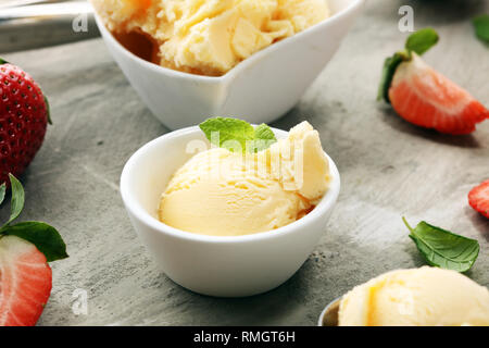 Gelato alla vaniglia scoop con fragole fresche e coni gelato su un sfondo rustico Foto Stock