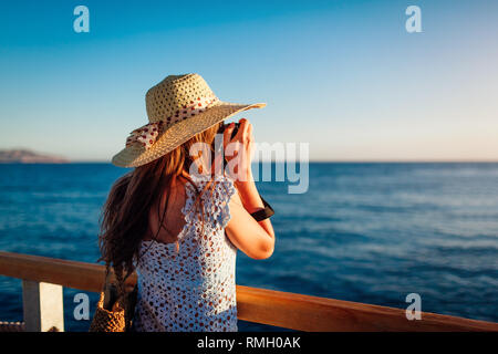 Giovane donna traveler per scattare delle foto del paesaggio di mare sul molo l'utilizzo della fotocamera. Moda estate. La vacanza estiva. Foto Stock