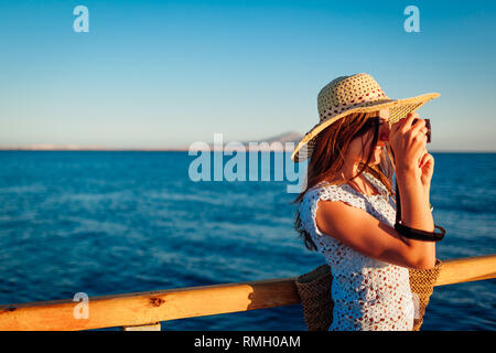 Giovane donna traveler per scattare delle foto del paesaggio di mare sul molo l'utilizzo della fotocamera. Moda estate. La vacanza estiva. Foto Stock