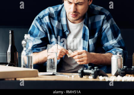 L'uomo soffre di sbornia tenendo l'aspirina e guardando il bicchiere di acqua Foto Stock