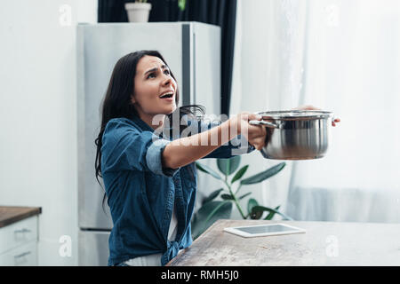 Preoccupato della donna in denim con breve pot che si occupano di acqua danno in cucina Foto Stock
