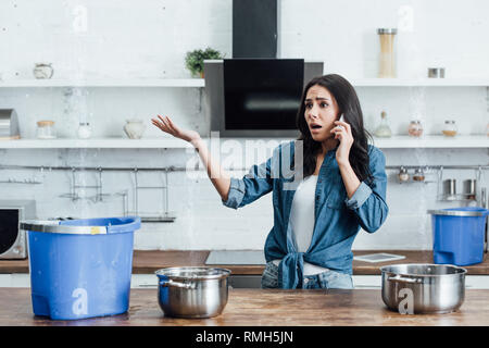 Preoccupato della donna alla ricerca di perdite di acqua dal soffitto e chiamando il idraulico Foto Stock