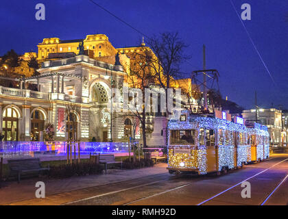 La luce di Natale di rotolamento del tram di fronte al giardino del castello Bazaar a Budapest presso il blue ora Foto Stock