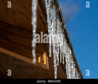 Primo piano di ghiaccioli sospesi dal tetto di una casa in legno su una soleggiata giornata invernale. Foto Stock