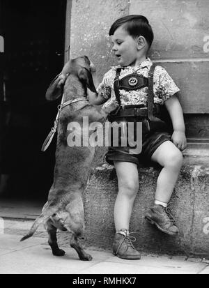 Ragazzo con Lederhosen alimenta un accattonaggio bassotto gelato Munich-Sendling. Foto Stock