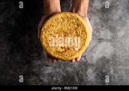 Elevato angolo di visione di un uomo caucasico con un tipico la tortilla de patatas, frittata spagnola, sulle sue mani su una pietra grigia superficie Foto Stock