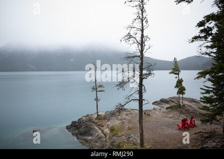 Due sedie rosse si affaccia sul Lago Minnewanka su un nebbioso giorno nel Parco Nazionale di Banff, Canada Foto Stock