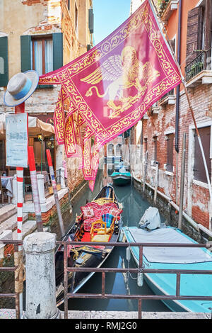 Gondola, barca e bandiera della regione italiana Veneto sul Canal Grande a Venezia presso la stazione della funivia, Italia. Tradizionale del gondoliere cappello di paglia su un po Foto Stock