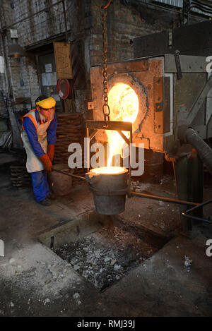 Foundrymen pour ferro fuso dal forno in un ladel. (Shot in luce disponibile con profondità di campo). Foto Stock