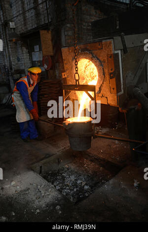 Foundrymen pour ferro fuso dal forno in un ladel. (Shot in luce disponibile con profondità di campo). Foto Stock