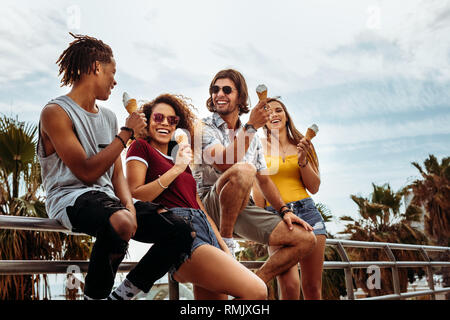 Amici appoggiata ad una ringhiera godendo di mangiare il gelato all'esterno. Allegro buddies mangiare gelato all'esterno. Foto Stock
