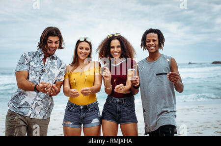 Happy amici festa sulla spiaggia con botti. Multi-etnico gruppo di amici in spiaggia per celebrare il capodanno. Foto Stock