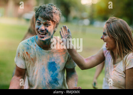 Giovane divertendosi holi in un parco con gli amici. Donna felice godendo holi applicando il colore per il suo fidanzato. Foto Stock