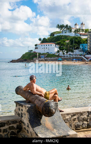 SALVADOR, Brasile - 13 Marzo 2015: un uomo brasiliano si rilassa su uno del cannone reliquie presso il Forte di Santa Maria affacciato sul Porto da Barra Beach. Foto Stock