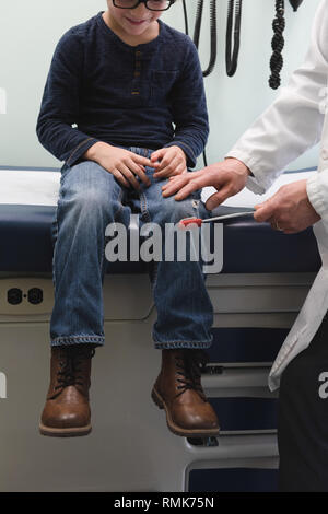 Giovani asiatici medico maschio esaminando caucasian boy il ginocchio del paziente in una clinica. Medico maschio utilizzando h reflex Foto Stock