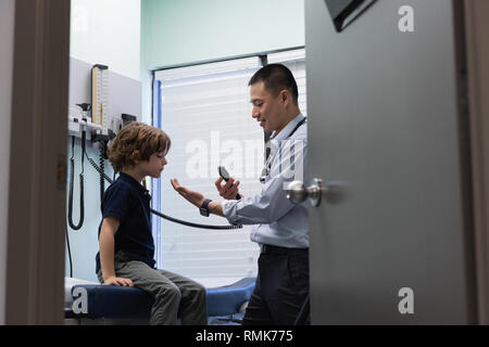 Giovani asiatici medico maschio esaminando un ragazzo caucasico paziente con lo strumento medicale Foto Stock