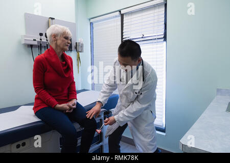 Giovani asiatici medico maschio esaminando un senior paziente con martello reflex Foto Stock