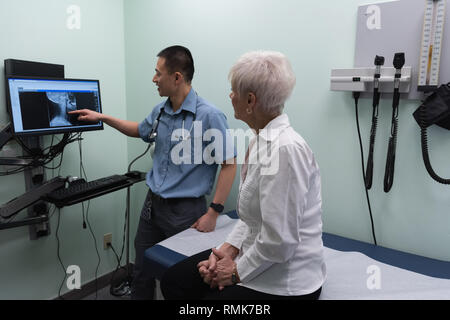 Giovani asiatici medico maschio discutendo su x-ray relazione sul computer presso la clinica Foto Stock