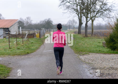 Vista posteriore di un accoppiamento giovane donna jogging lungo una strada rurale in inverno in una giornata grigia in uno stile di vita sano e concetto di fitness Foto Stock