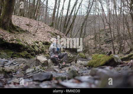Giovane uomo russo escursionismo in Sochi Parco Nazionale: appoggio seduto su una roccia nei pressi del fiume Foto Stock