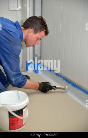 Tradesman pittura bordo del pavimento prima linea prodotto epossidico è utilizzato in un edificio industriale Foto Stock