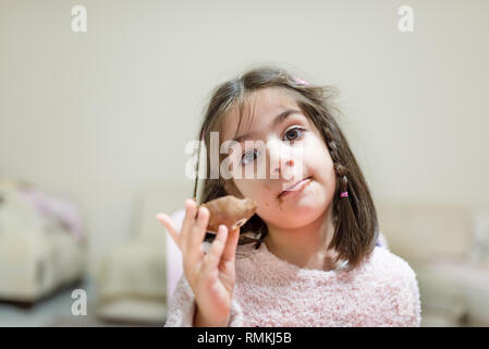 Poco carino ragazza mangia la sorpresa di cioccolato con faccia buffa mentre guardando la fotocamera Foto Stock