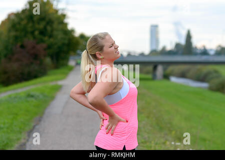 Giovane donna bionda di indossare abbigliamento sportivo tenendo le sue dolorose indietro mentre ti alleni all'aperto Foto Stock