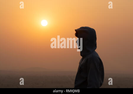 In prossimità di una persona stancato felpa con cappuccio in piedi sopra la montagna con sfondo al tramonto Foto Stock