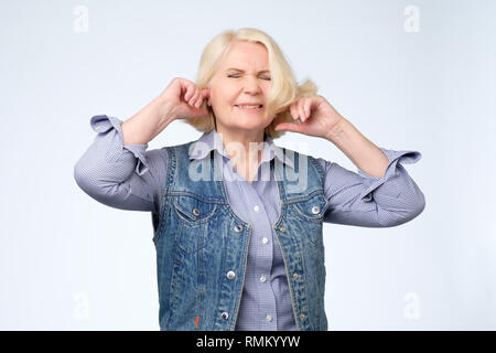 Infelice ha sottolineato senior rendendo femmina wry face, collegando le orecchie con le dita Foto Stock