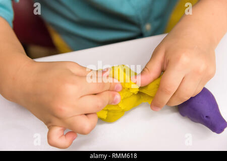 Quattro anni ragazzo caucasico rende le mani con figure di animali provenienti da tecniche di modellizzazione argilla gialla sul piano portapaziente in bianco. Bambini creatività educazione prescolare hobby Foto Stock