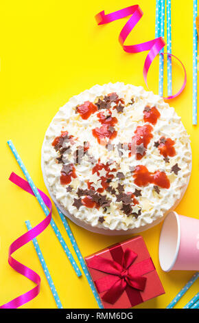 Strato di spugna torta di compleanno con panna montata di glassa di cioccolato al latte star spruzza confettura di fragole. Modello in carta rosa bicchieri cannucce blu confezione regalo su Foto Stock